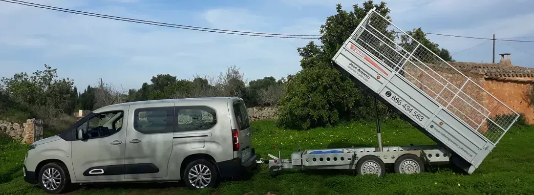Camioneta plateada remolcando un pequeño remolque con un gran panel blanco inclinado en un campo de hierba.