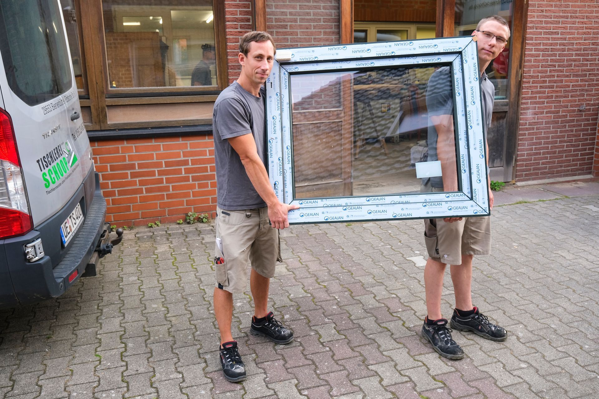 Zwei Männer halten ein großes Fenster vor einem Lieferwagen.