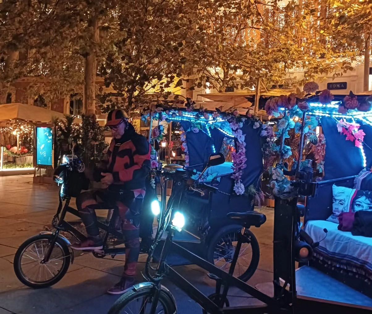 Un hombre va en bicicleta junto a un rickshaw por la noche.