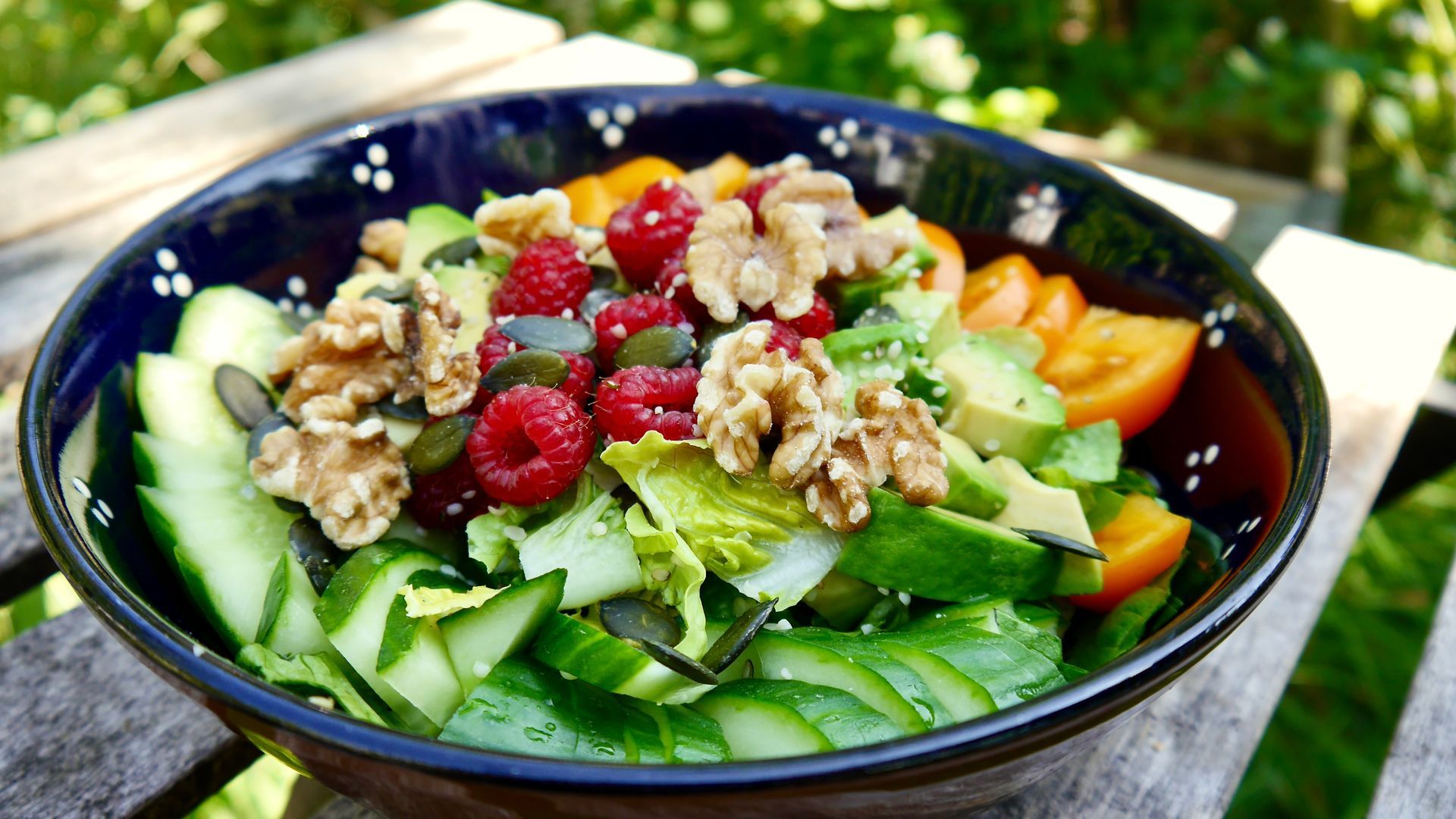 Eine Schüssel Salat mit Himbeeren, Walnüssen, Gurken und Tomaten auf einem Holztisch.