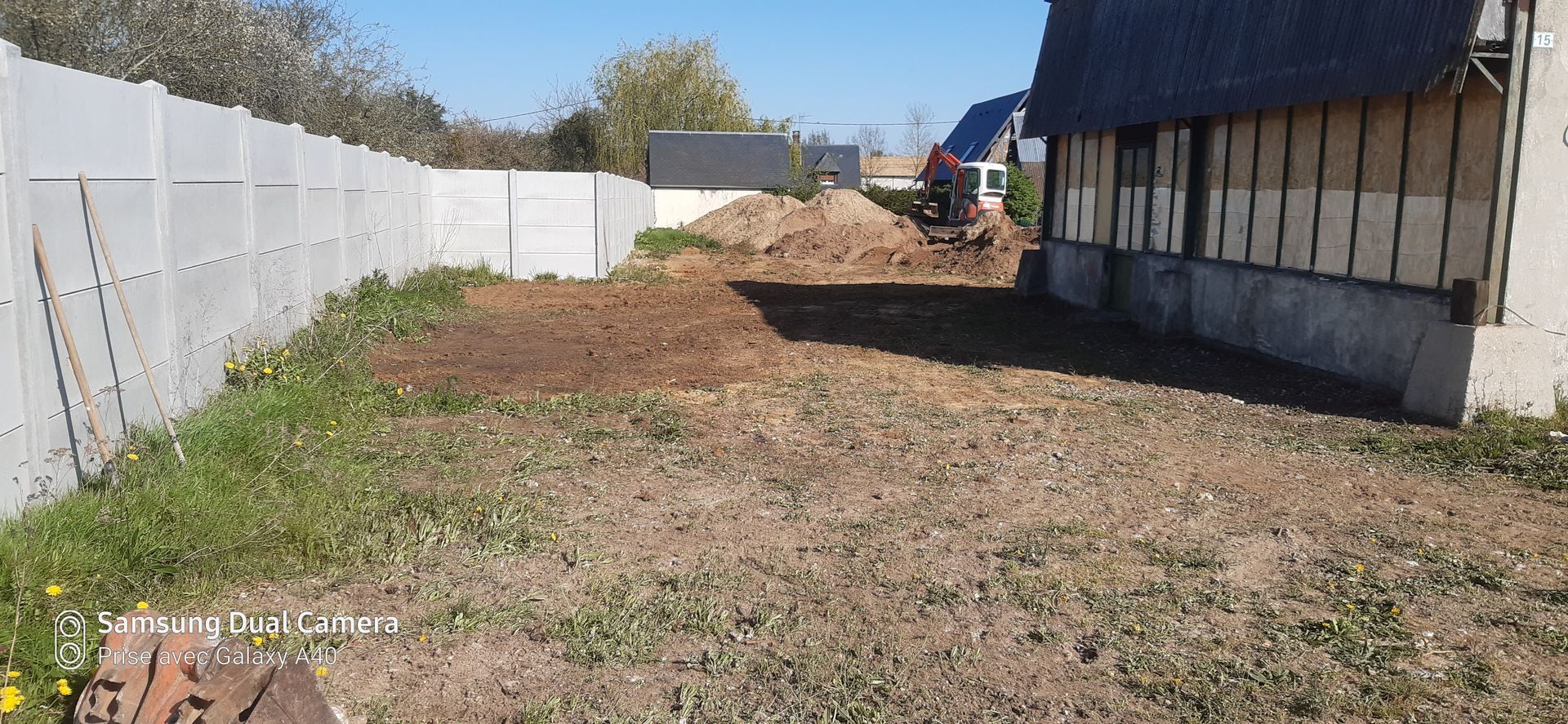 Terrain en terre avec quelques brins d'herbe, et un engin de chantier au fond