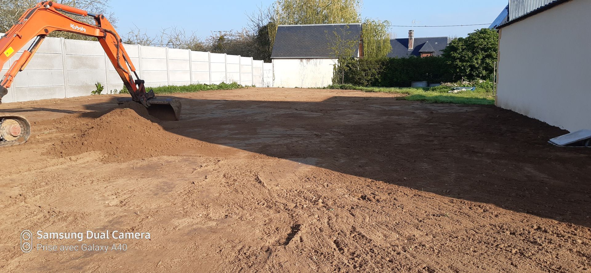 Pelleteuse qui creuse le sol d'un terrain en terre avec des palissades blanches