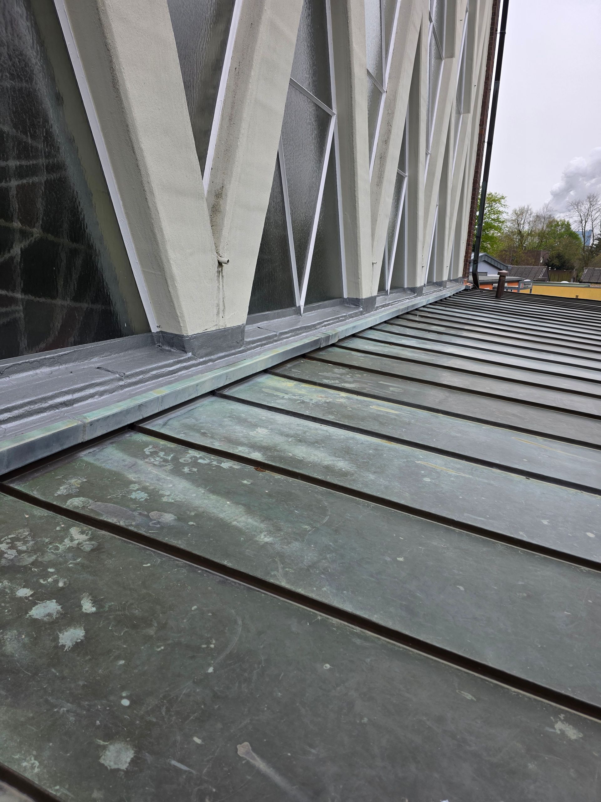 Nahaufnahme eines schrägen Metalldachs neben einem Gebäude mit schrägen weißen Fensterrahmen.