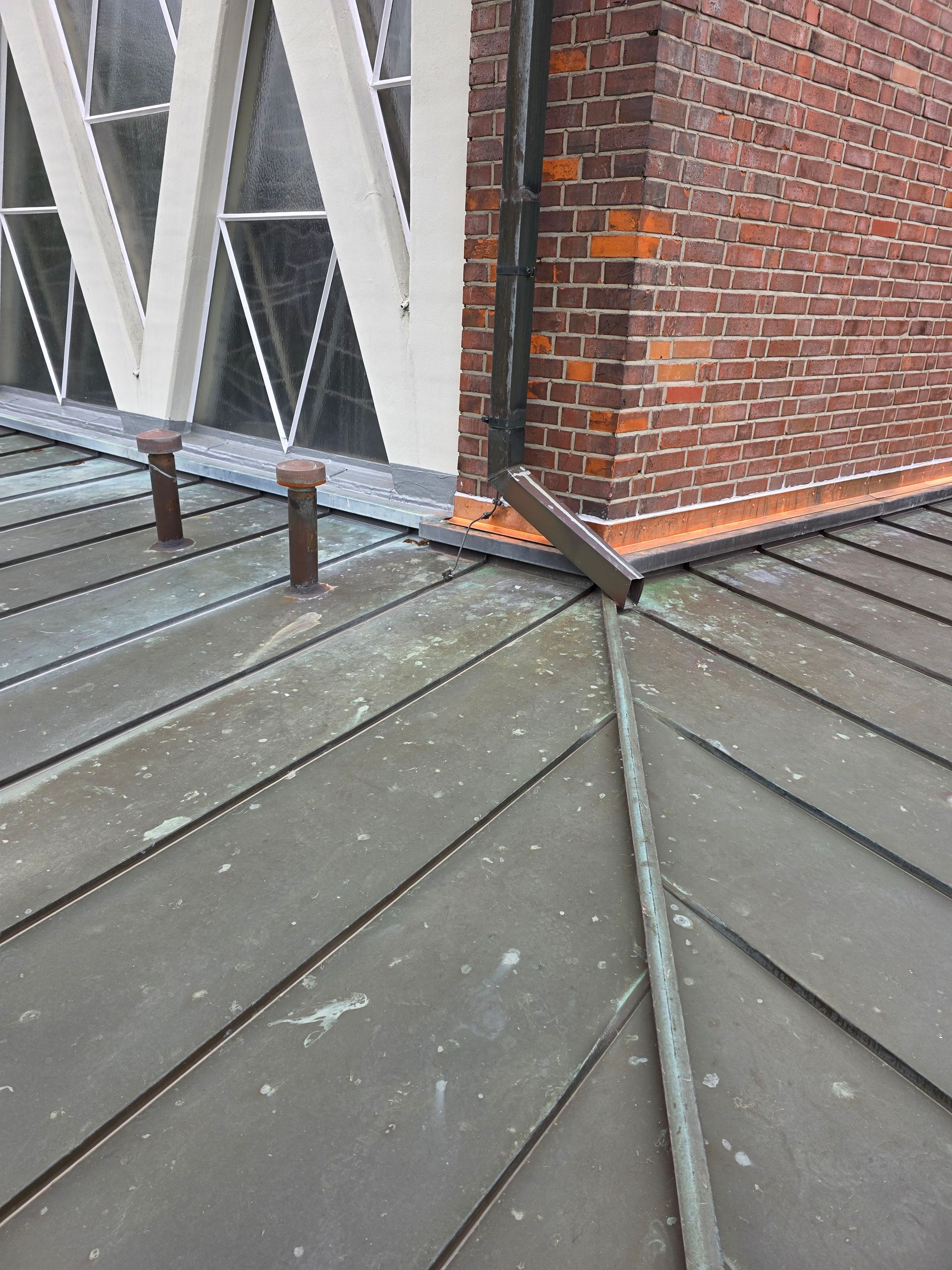 Dachterrasse mit grauen Metallpaneelen, Backsteinmauer und weißen dreieckigen Fensterrahmen.