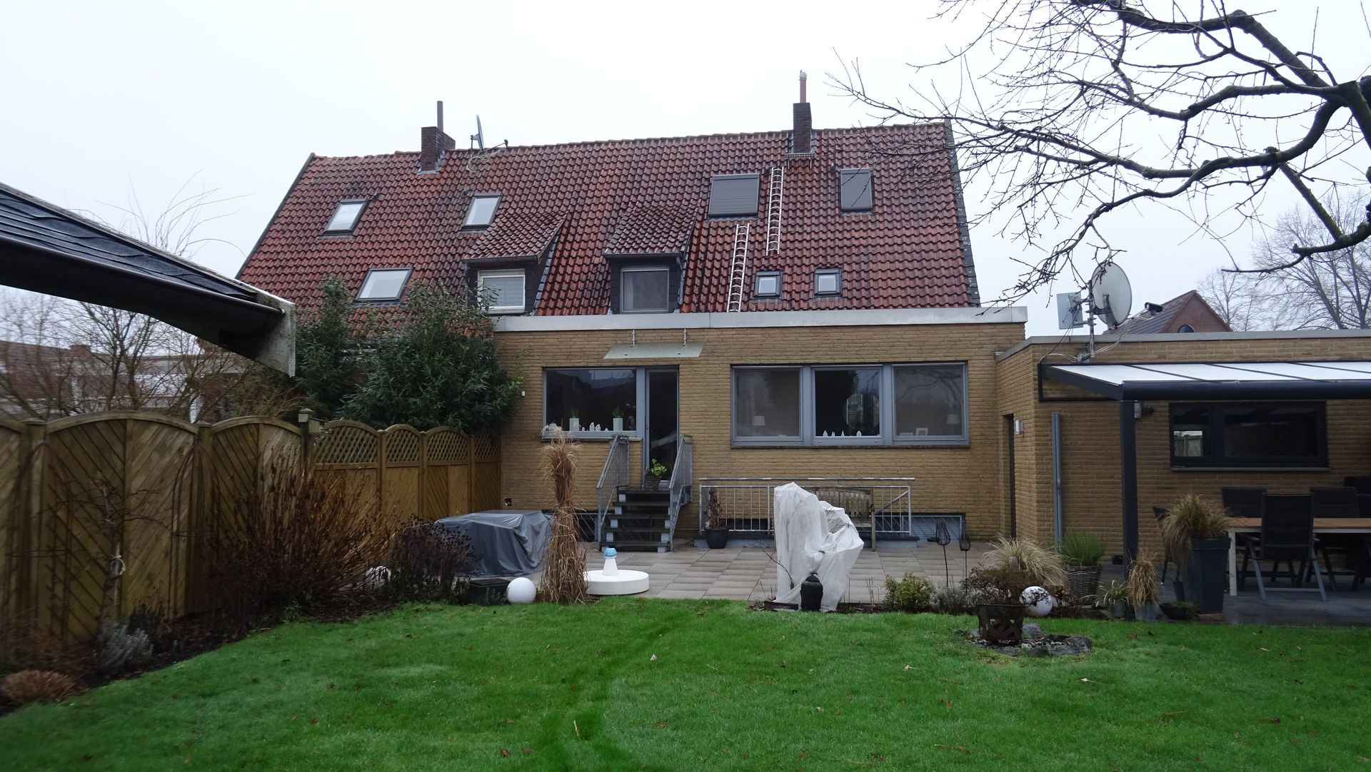 Hinterhof mit grünem Rasen, Terrassenmöbeln und einem Backsteinhaus mit rotem Ziegeldach im Winter.