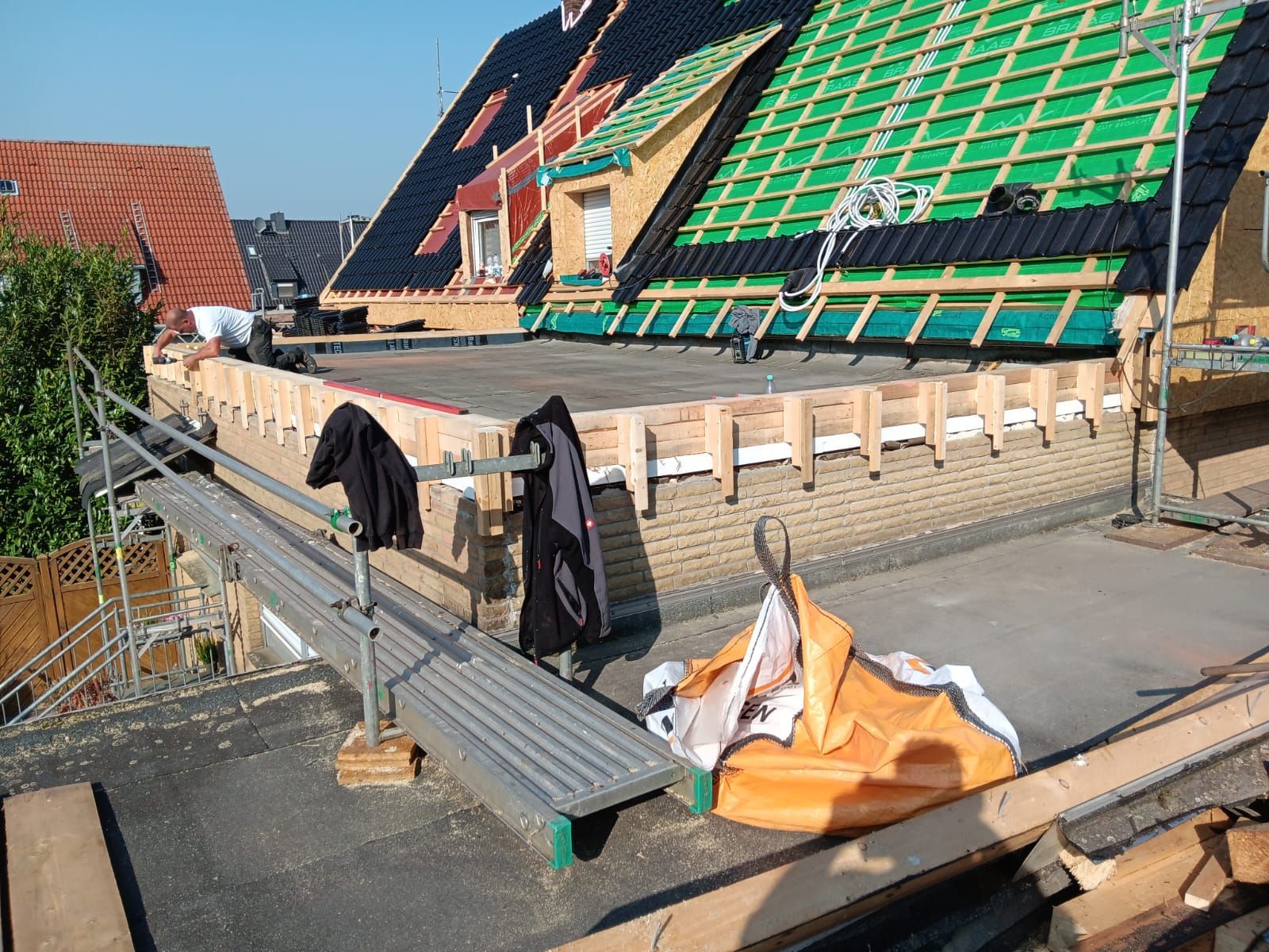 Das Dach befindet sich im Bau und ist mit grüner Verkleidung, Balken, Leitern und Arbeitern auf einem Gerüst versehen.