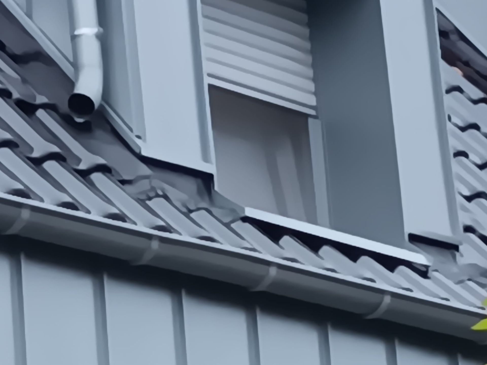 Graues Ziegeldach mit Dachgauben und Fallrohr an der Hausfassade