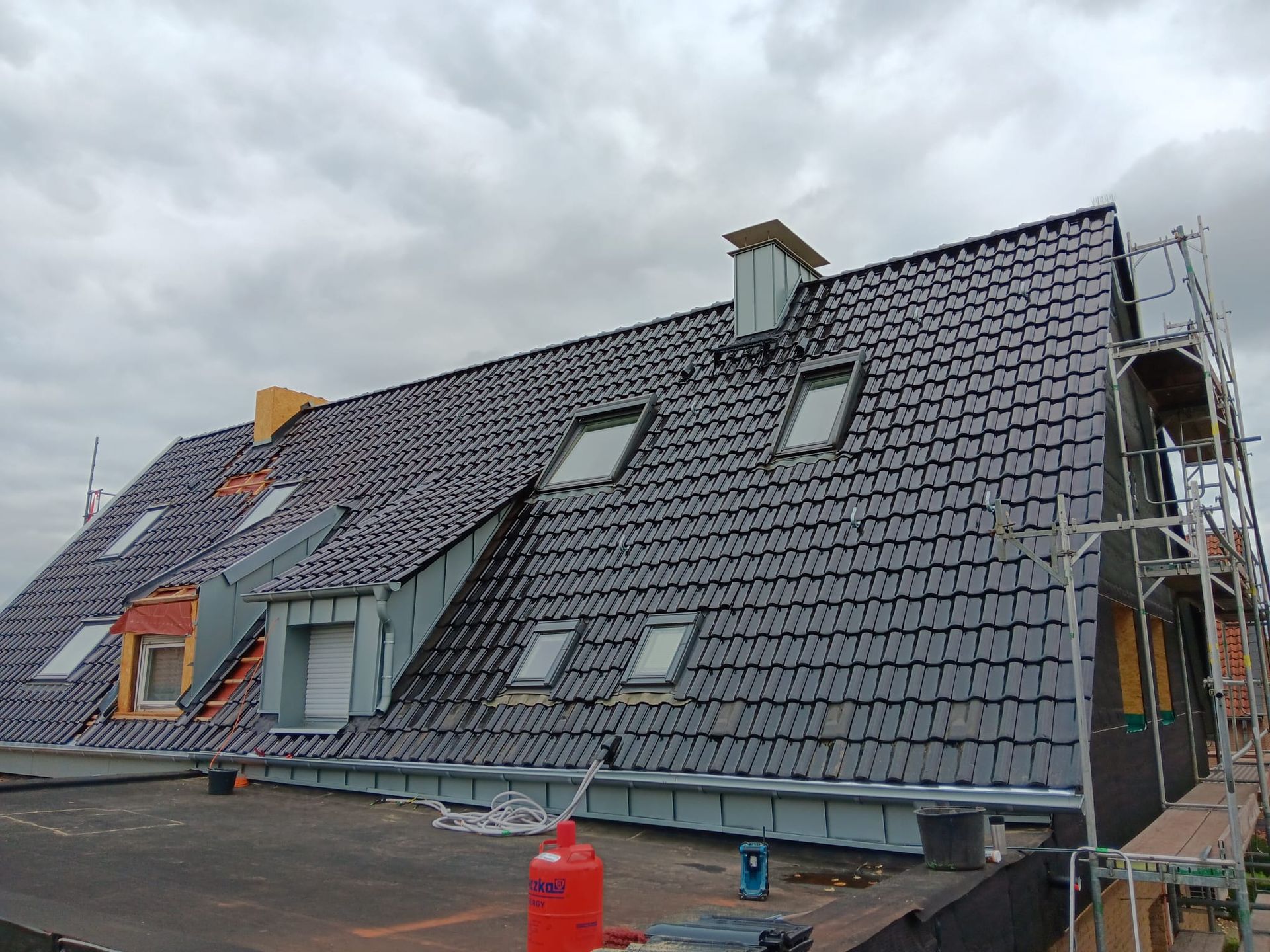 Das Dach ist im Bau und besteht aus dunkelgrauen Ziegeln, Dachgauben und einem Gerüst auf der rechten Seite.