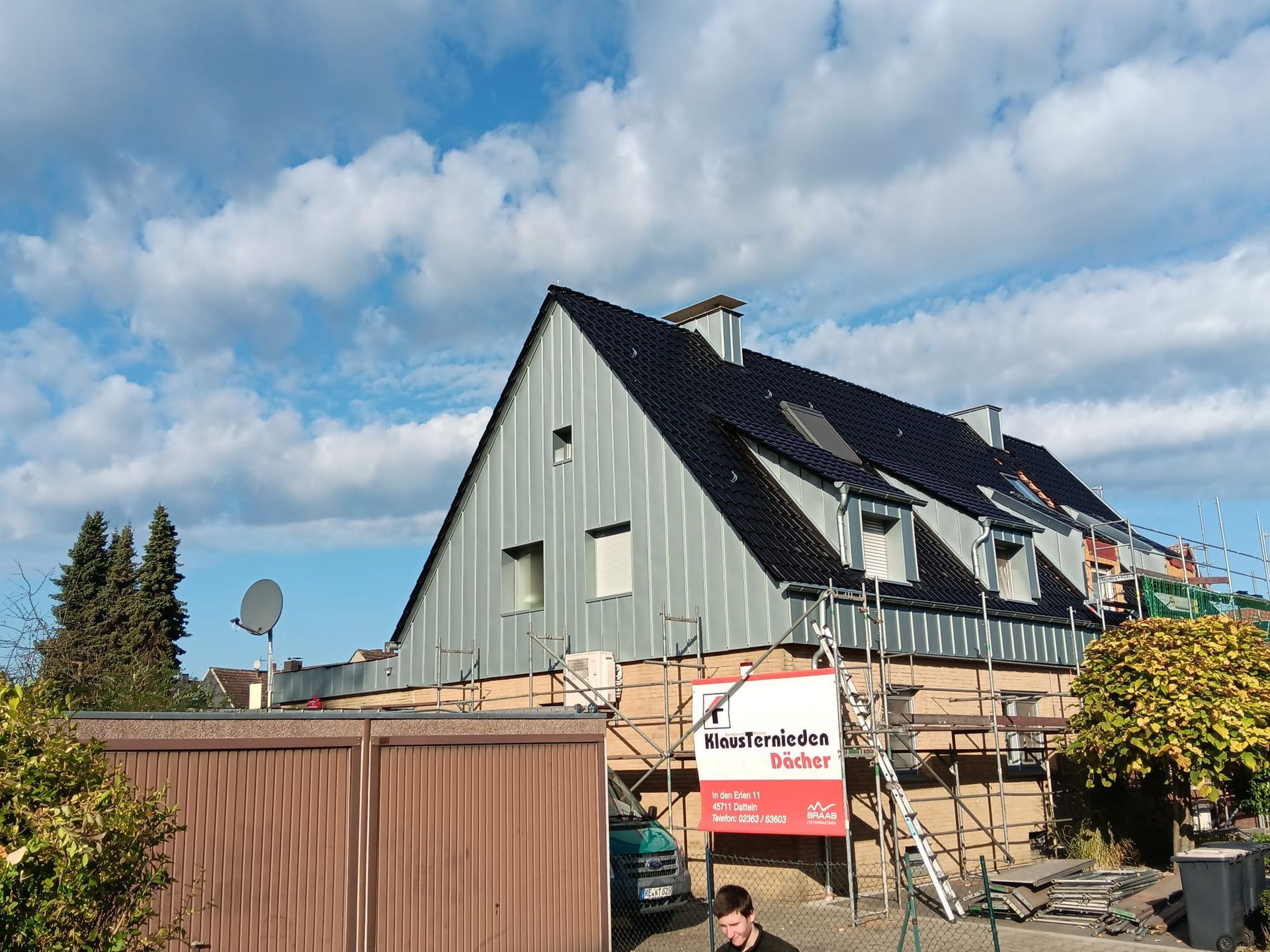 Giebelhaus im Renovierungszustand mit Gerüst, braunem Zaun und rotem Schild an einem sonnigen Tag
