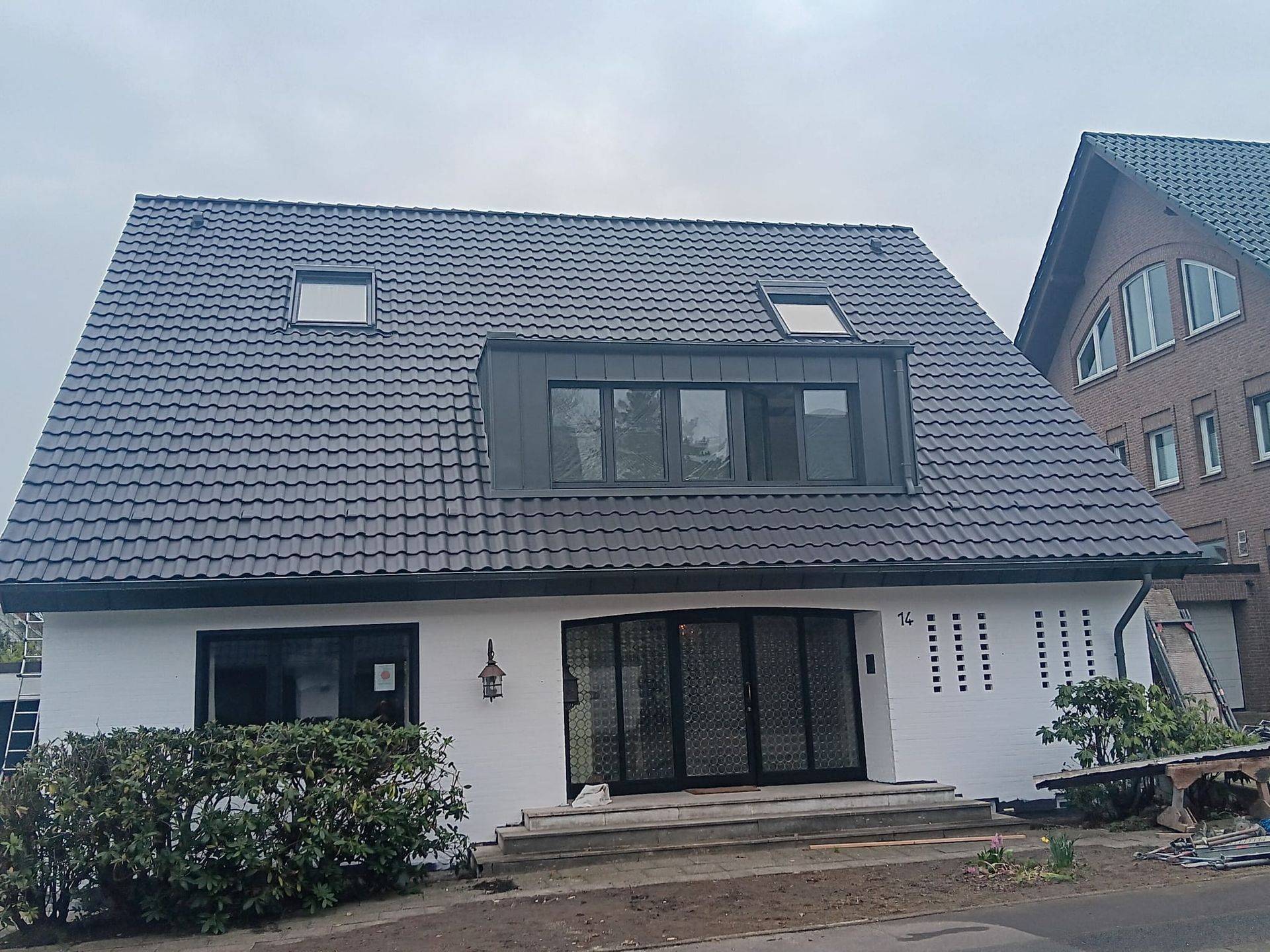 Modernes zweistöckiges weißes Haus mit dunkelgrauem Ziegeldach und großen Fenstern zur Straßenseite