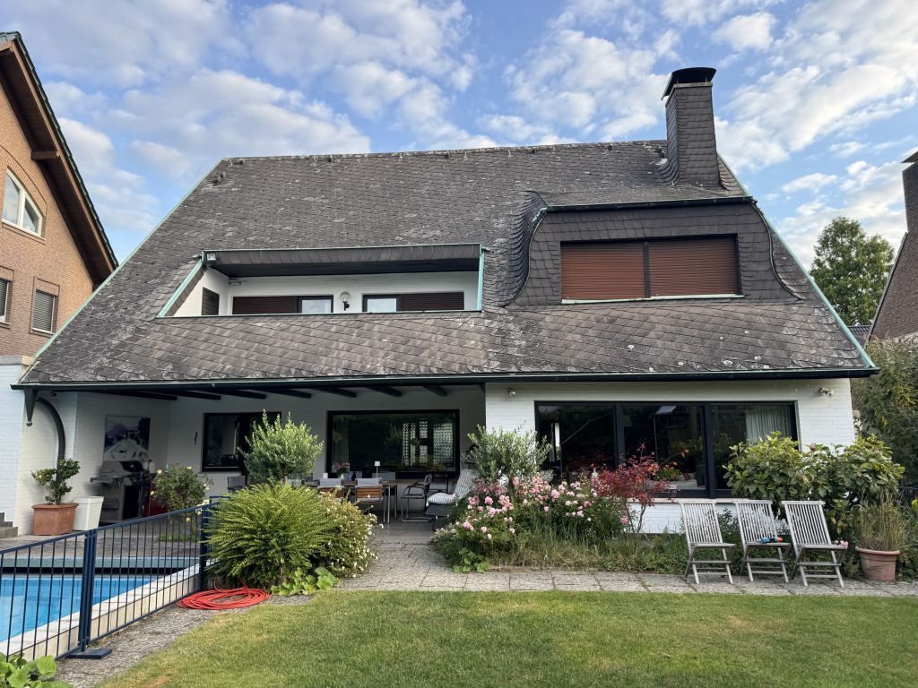 Modernes Haus mit überdachter Terrasse, Garten und Essbereich im Freien unter bewölktem Himmel