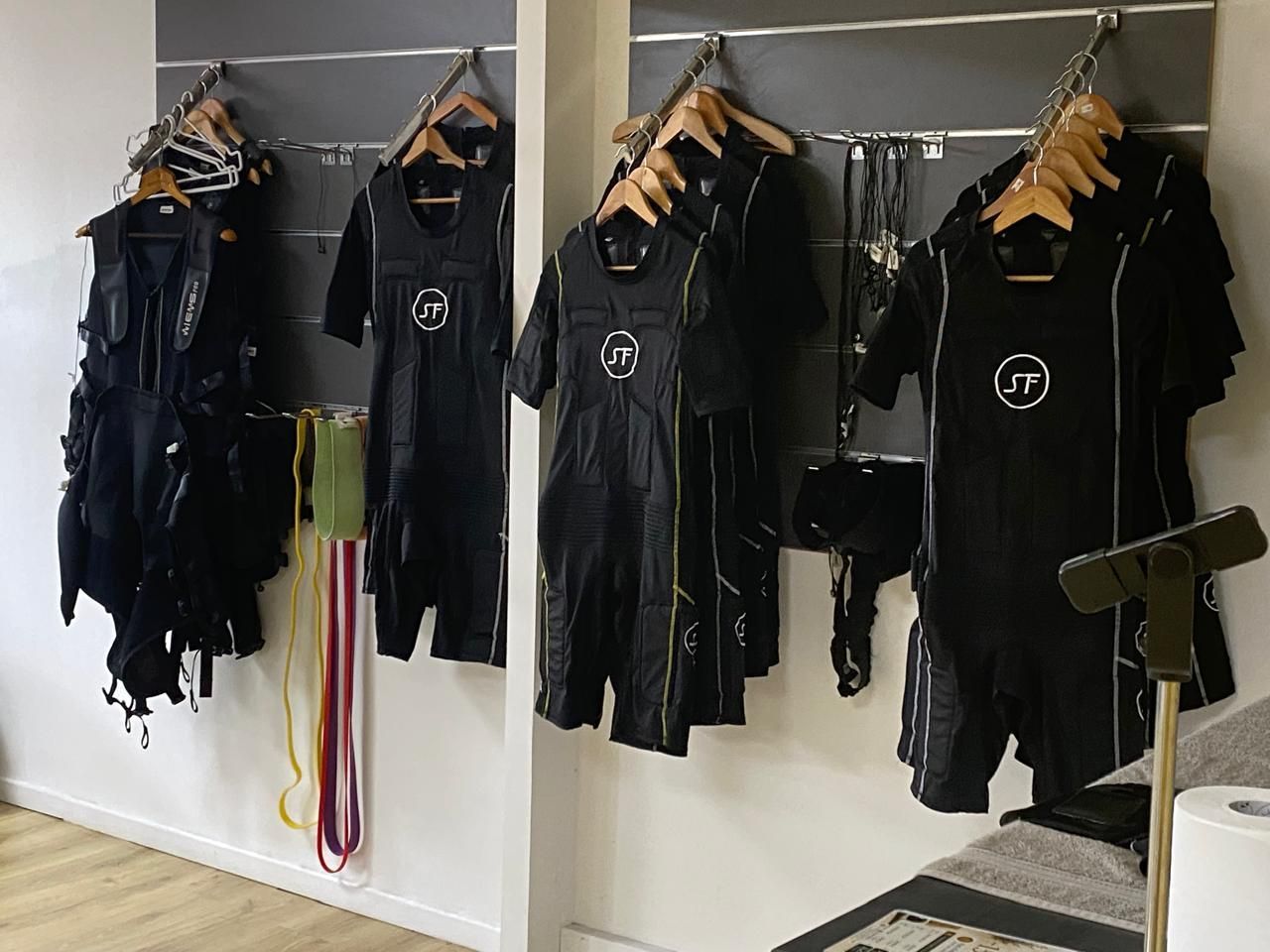 Des portants muraux avec des uniformes noirs et des cordons suspendus dans une salle d'entraînement.