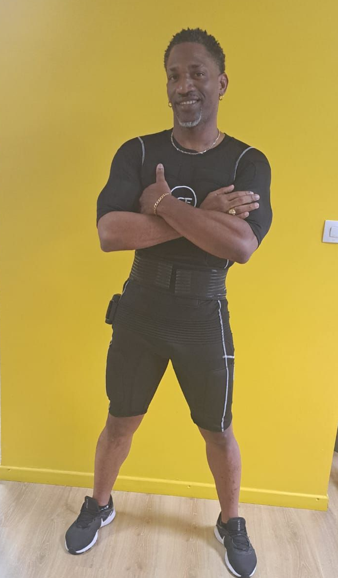 Deux personnes en tenues de fitness noires utilisent des appareils de musculation dans une salle de sport lumineuse.