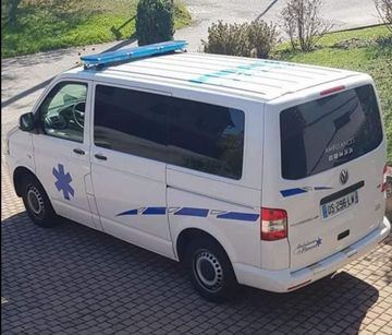 Fourgon ambulance blanc stationné sur une allée en briques, vu de dessus, avec des marquages d’urgence bleus.