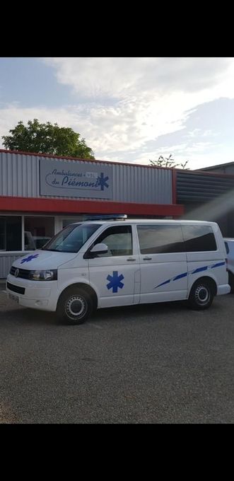 Fourgon blanc orné d’une étoile médicale bleue garé devant un bâtiment au crépuscule.