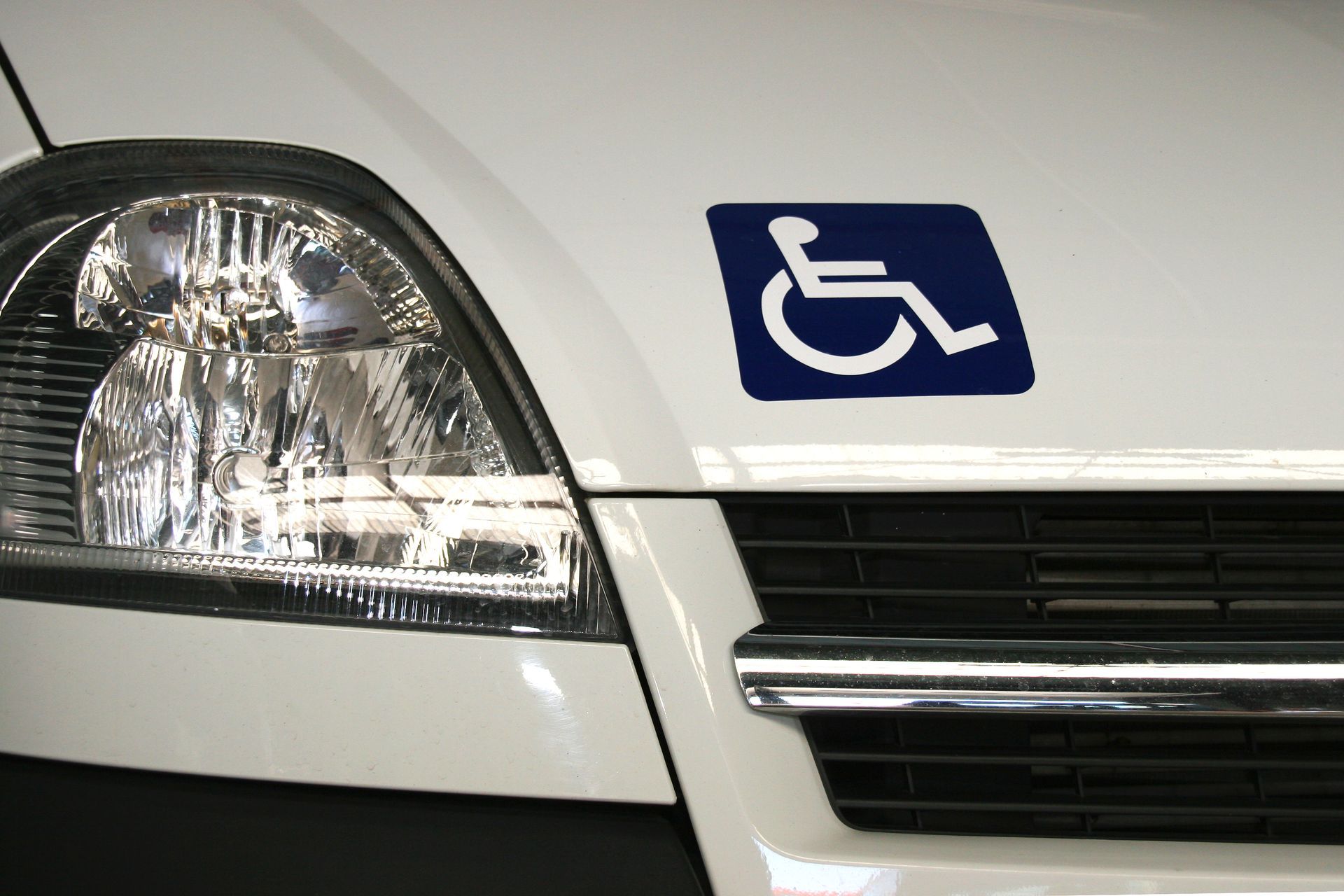 Panneau bleu d’accessibilité aux fauteuils roulants sur un véhicule blanc, près du phare.