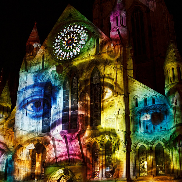 La façade de la cathédrale est illuminée par des projections colorées, notamment des yeux.