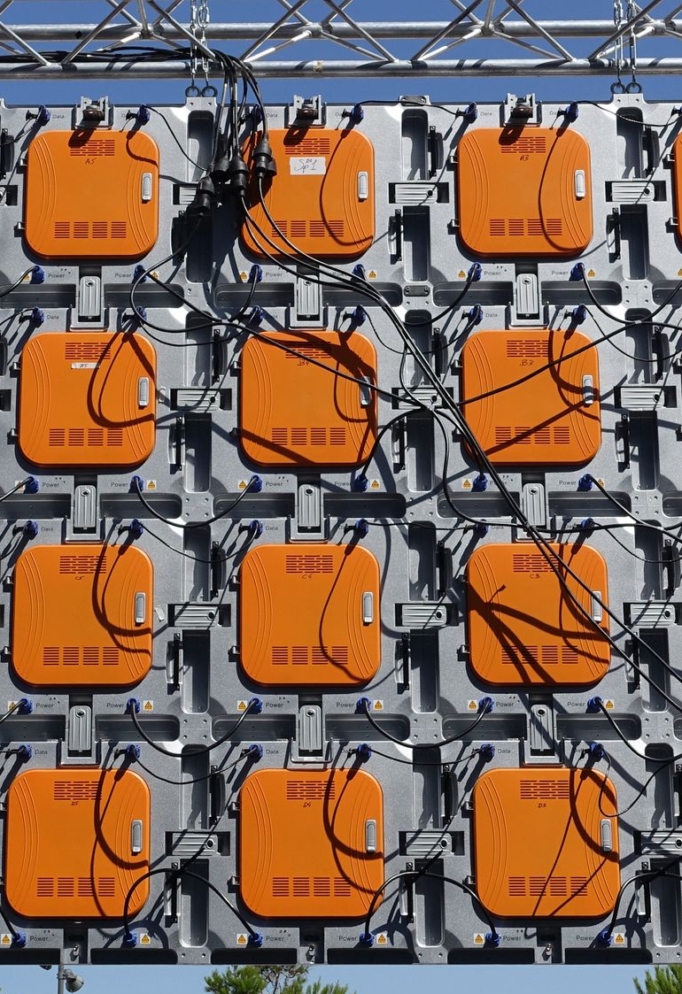 Gros plan sur une grille de panneaux carrés orange, reliés par des fils, sur un support métallique argenté.