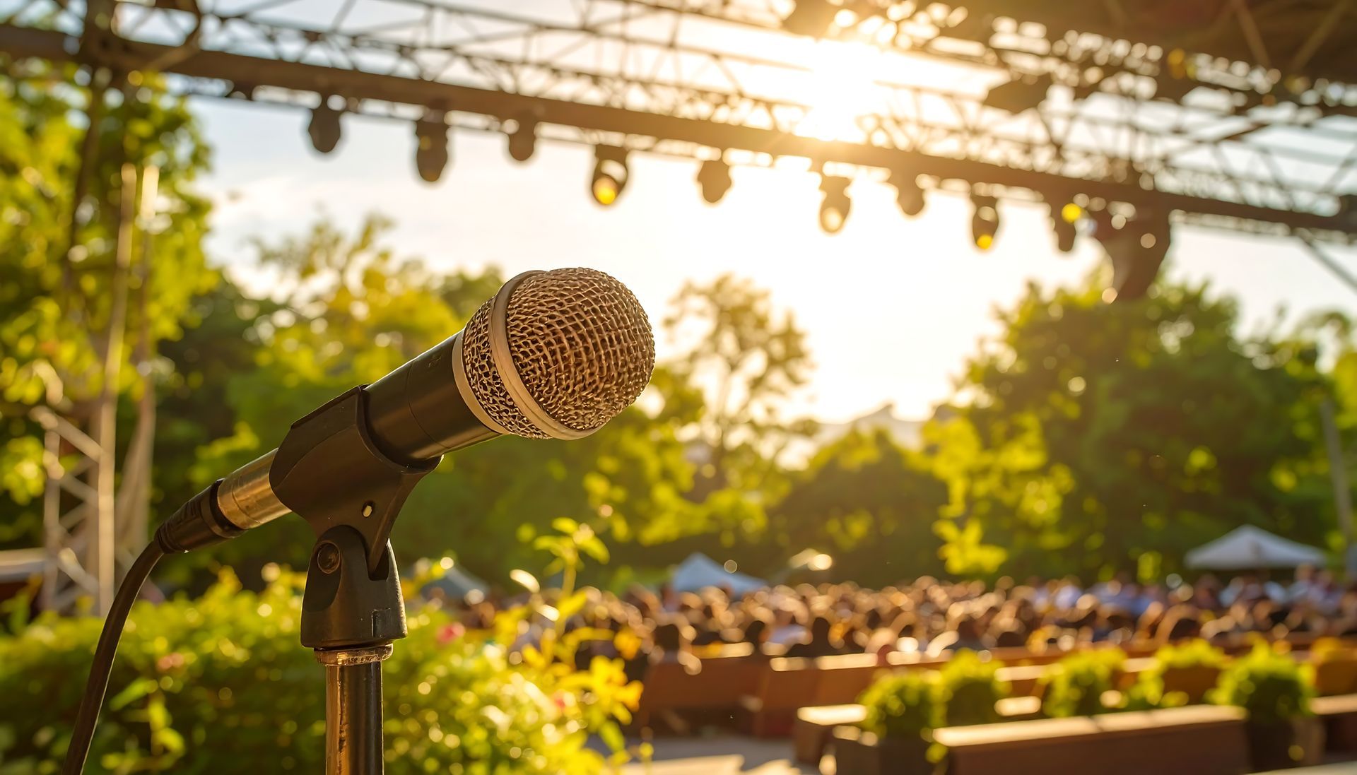 Microphone sur scène, concert en plein air ; foule ensoleillée en arrière-plan.