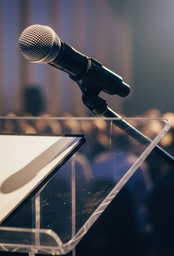 Microphone sur un podium transparent, avec un public flou en arrière-plan.