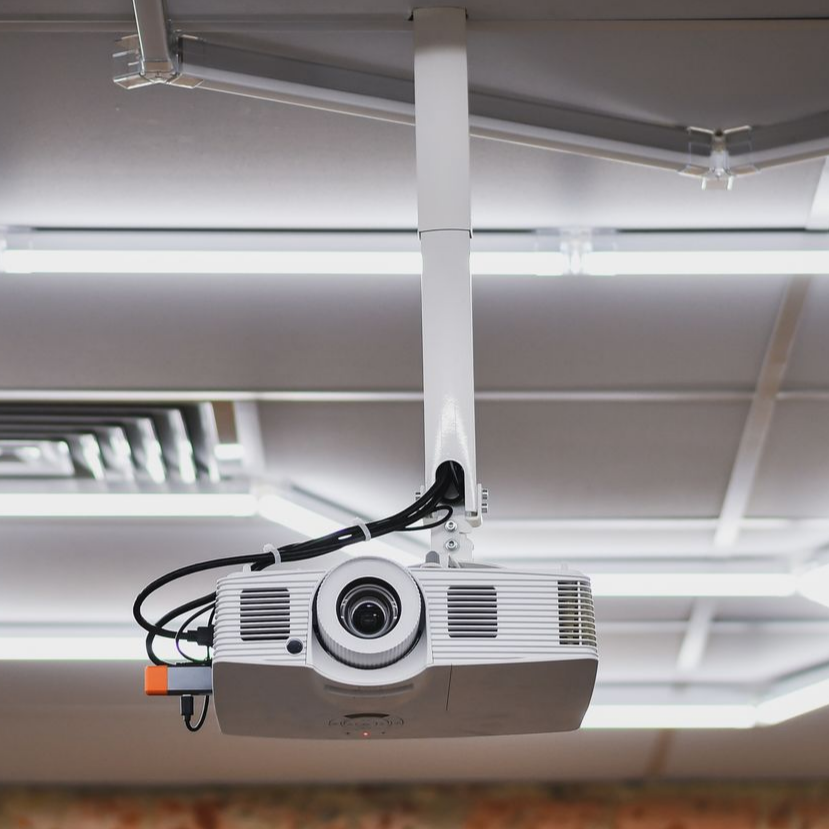 Un projecteur blanc est suspendu au plafond, des fils sont connectés, dans une salle de classe.