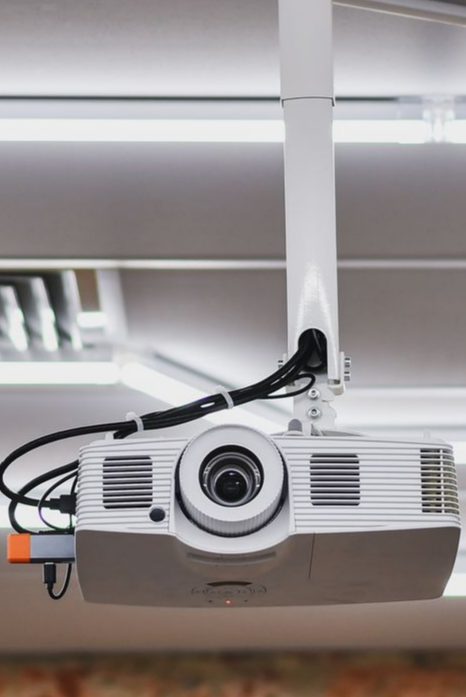 Projecteur blanc suspendu à un plafond blanc, câbles visibles, objectif orienté vers l'avant.