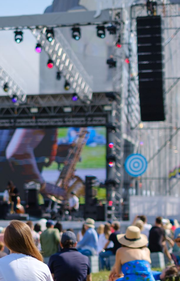 Scène de concert avec grand écran vidéo ; le public assiste au spectacle en plein air par une journée ensoleillée.