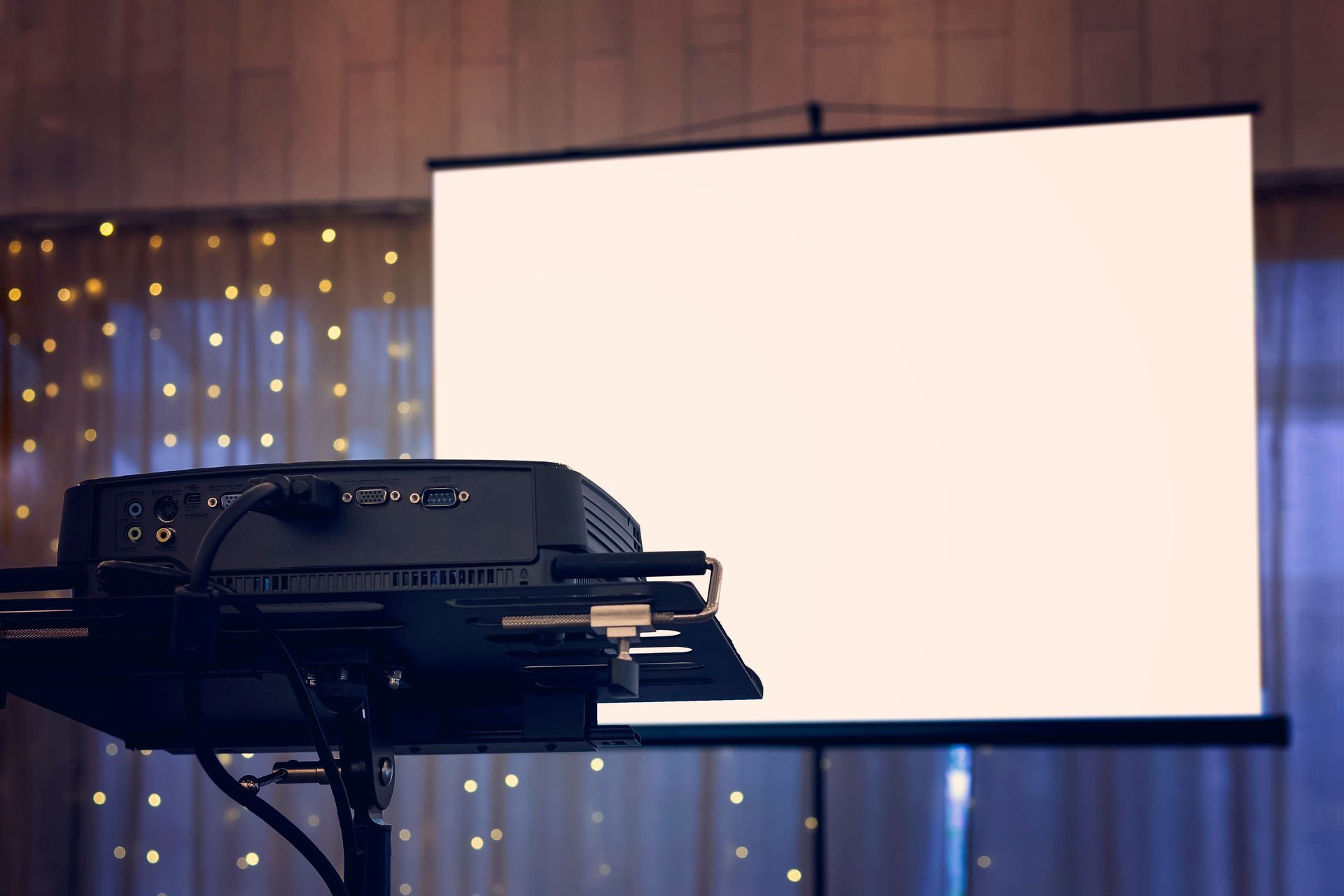 Un projecteur, fixé sur un trépied, projette une image sur un écran blanc. Fond éclairé.