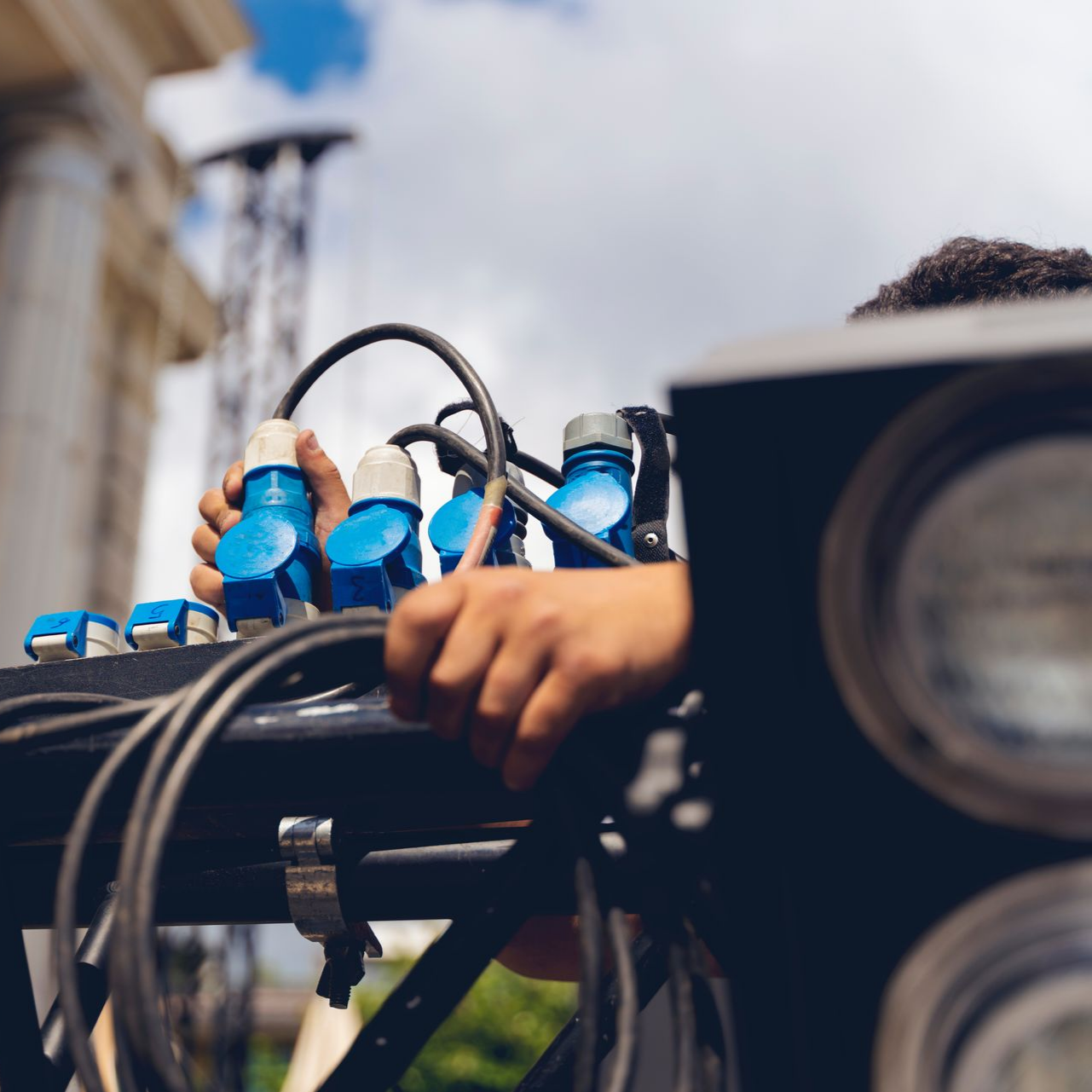 Personne connectant des câbles d'alimentation bleus à un projecteur de scène noir ; à l'extérieur.