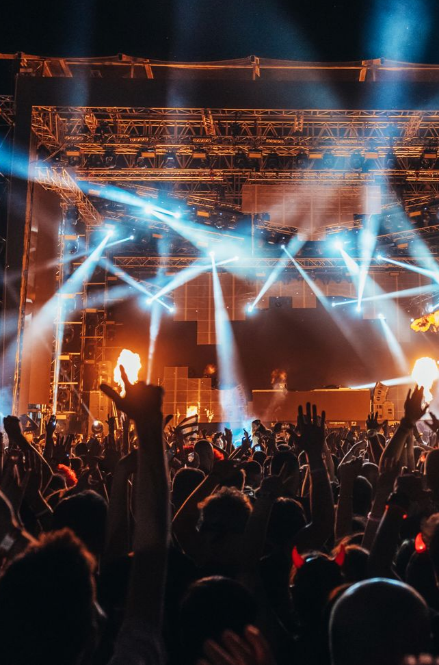 Le public du concert lève les mains en direction d'une scène illuminée par des projecteurs.