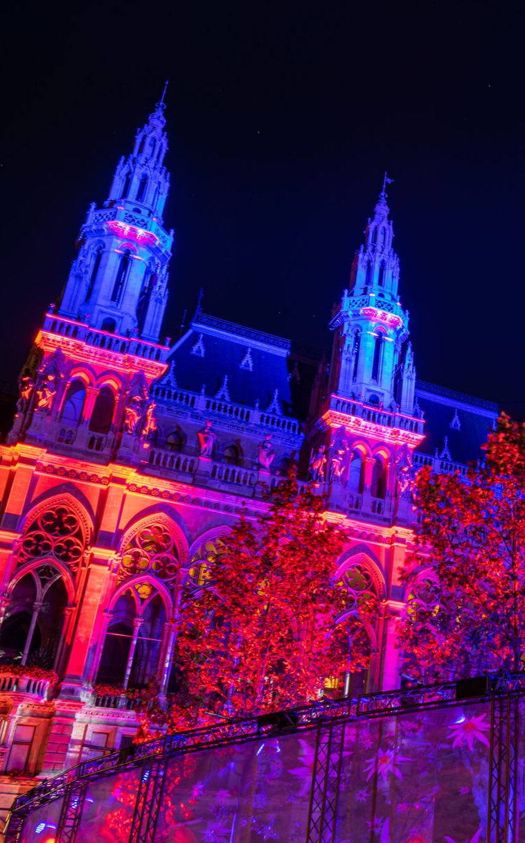 Vue nocturne d'un bâtiment illuminé de lumières rouges et bleues, avec deux hautes flèches.