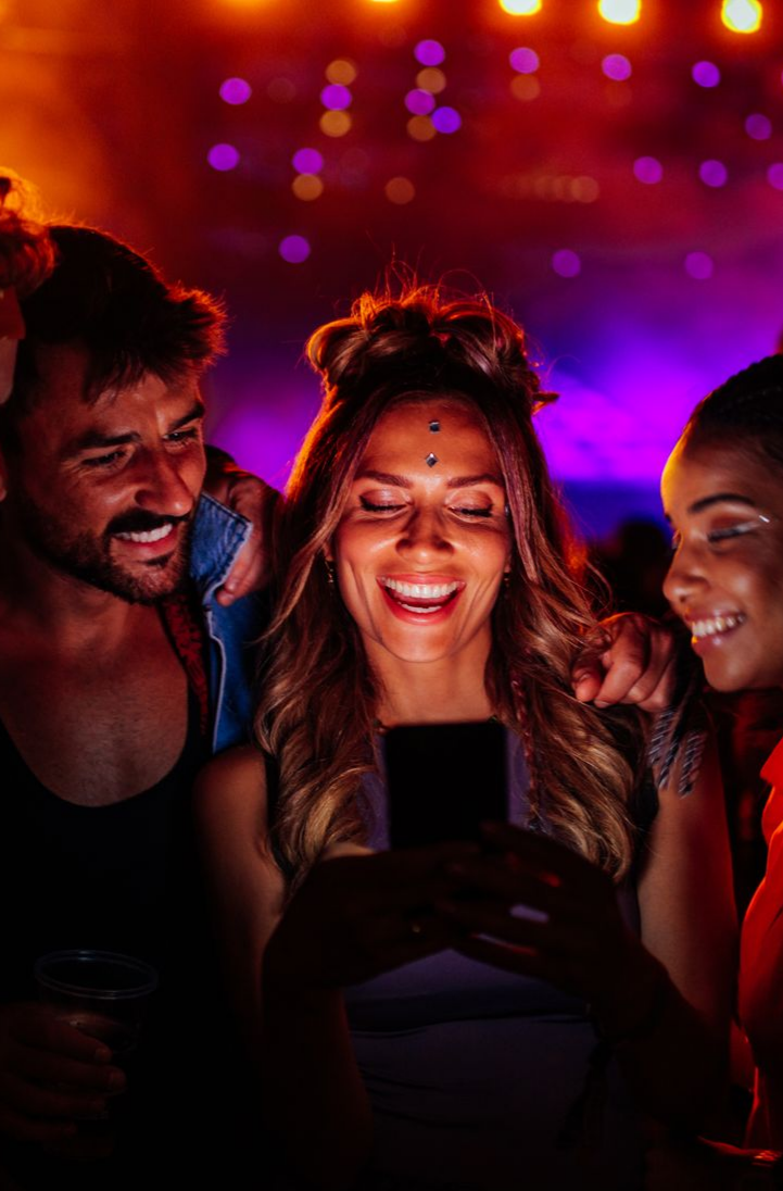 Trois personnes souriantes, regardant un téléphone portable avec des lumières colorées.