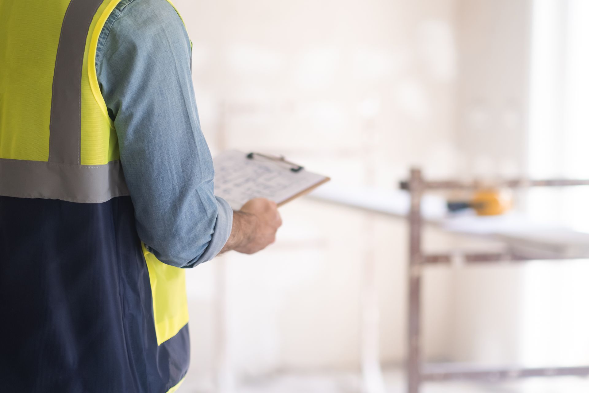Ouvrier du bâtiment portant un gilet réfléchissant et tenant un bloc-notes, inspectant un bâtiment.