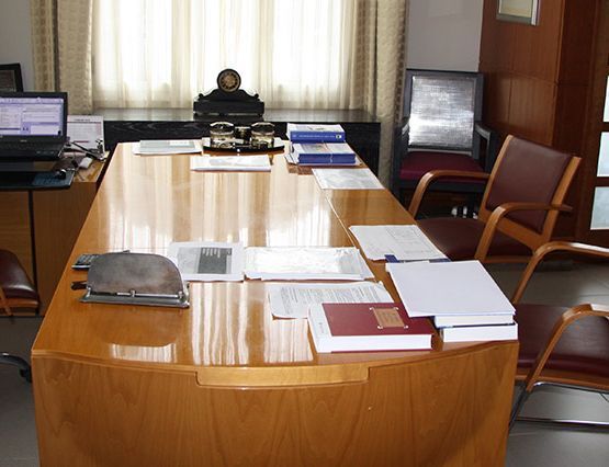 Una mesa larga de madera con papeles y una computadora portátil sobre ella.