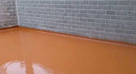 Suelo de epoxi color naranja en una habitación con paredes de ladrillo gris.