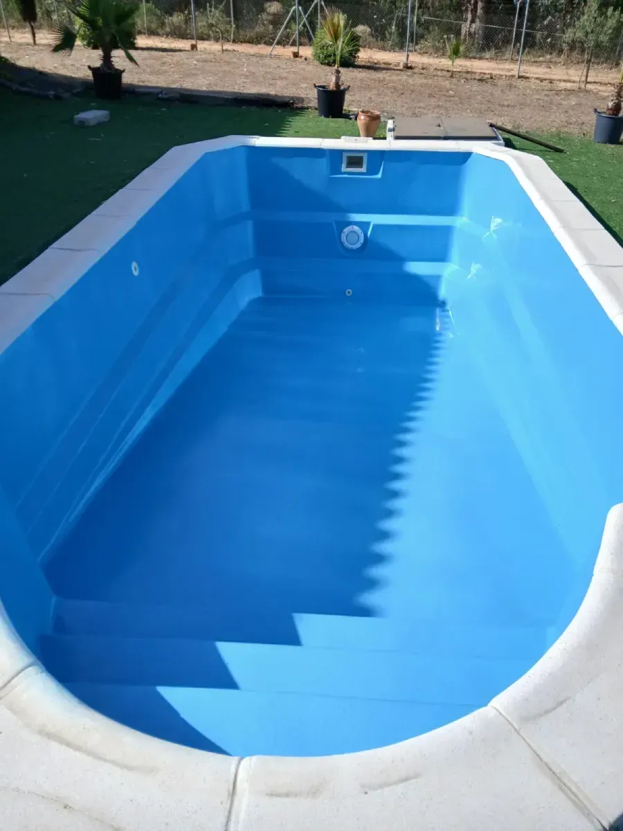 Piscina rectangular vacía con interior azul, borde blanco y escalones.