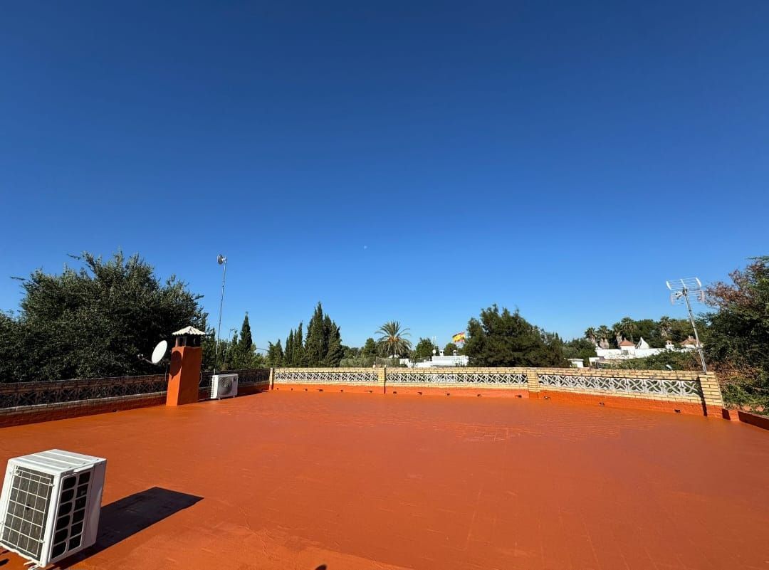 Azotea naranja con aires acondicionados, chimenea y árboles contra un cielo azul.
