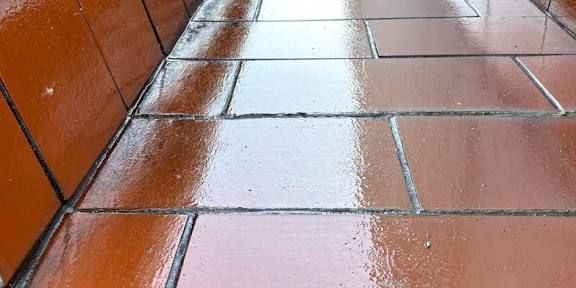 Suelo de terracota húmedo y brillante. Líneas de lechada oscuras. Pared naranja al fondo.