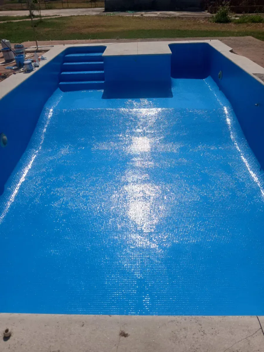 Piscina azul con superficie texturizada, escalones y borde de hormigón, al aire libre.