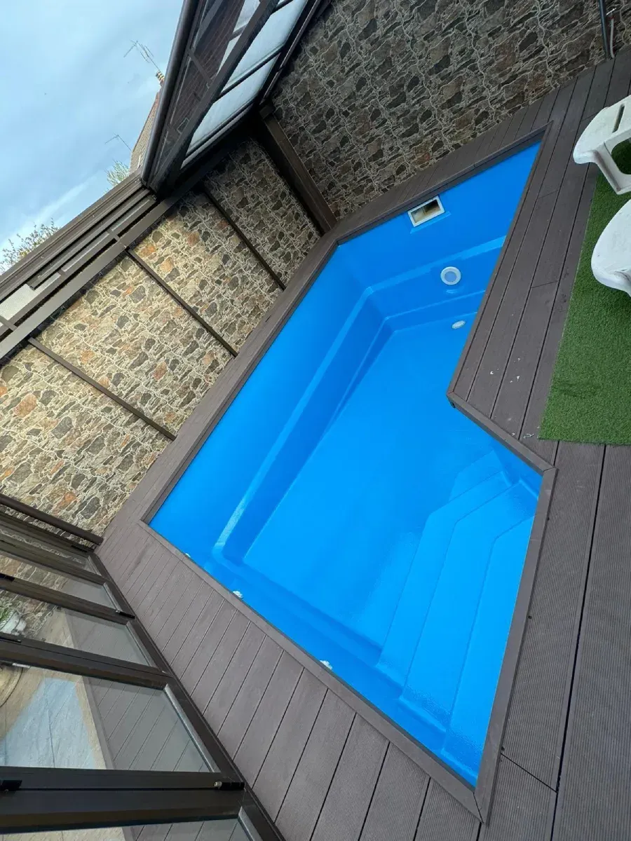 Pequeña piscina azul con cubierta de madera marrón y pared de piedra.