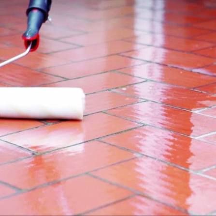 Un rodillo de pintura aplica un sellador brillante a las baldosas rojas del piso.