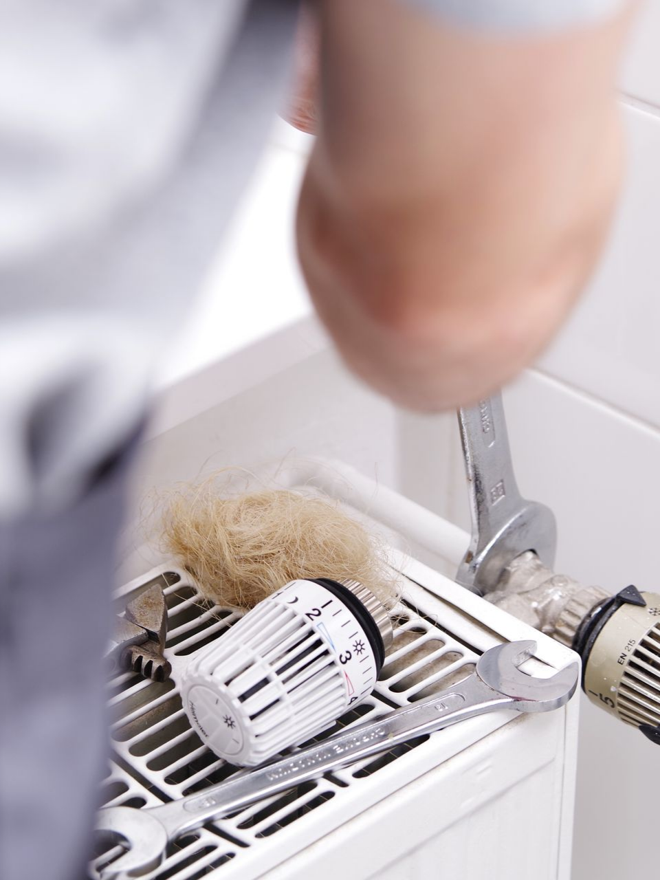 Personne utilisant des clés pour travailler sur un radiateur blanc.