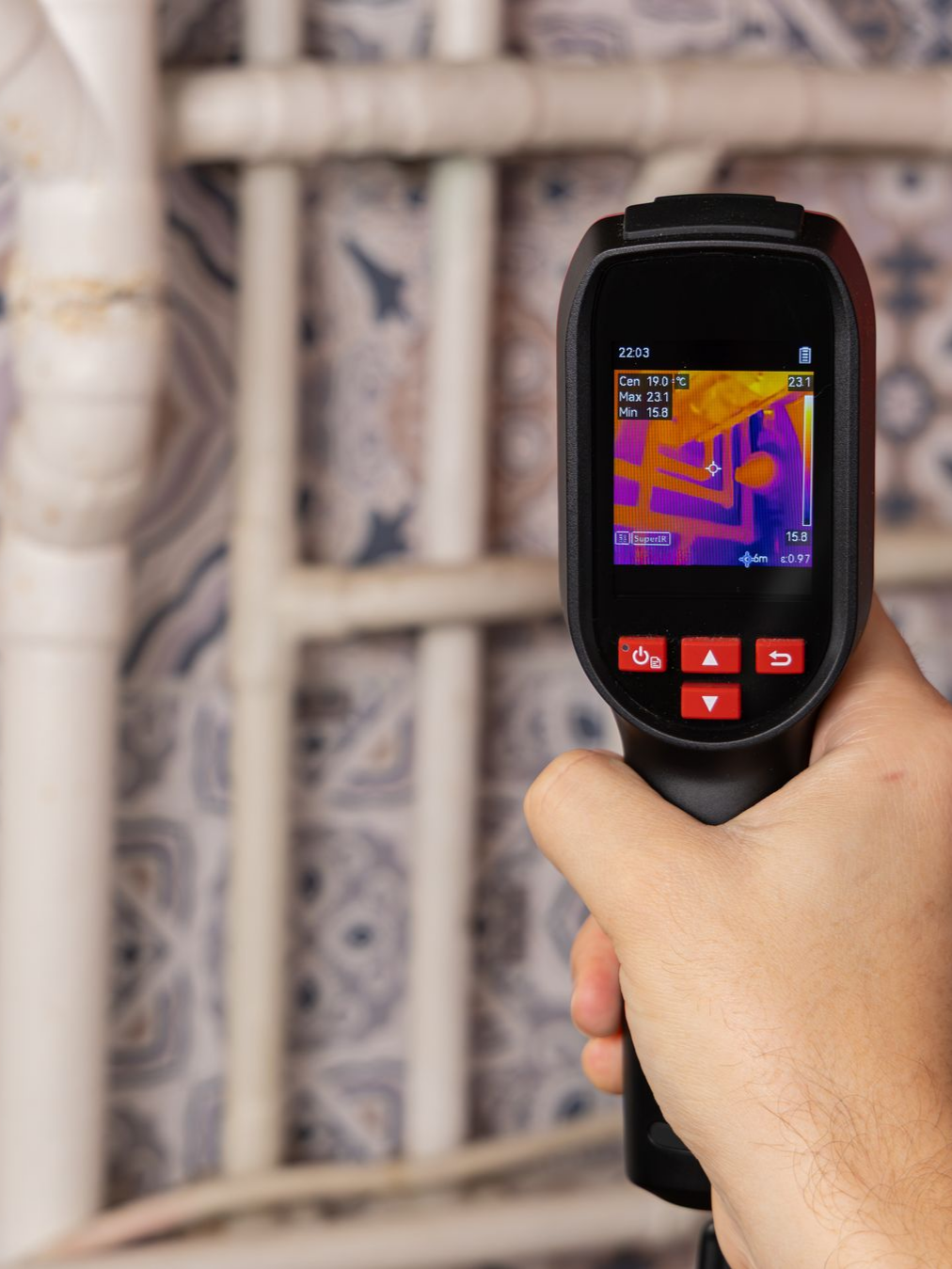 Main tenant une caméra thermique pointée vers des canalisations.