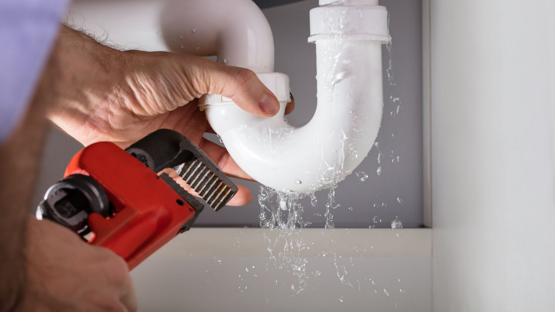 Un plombier utilise une clé pour réparer une fuite sur un tuyau blanc sous un évier. 