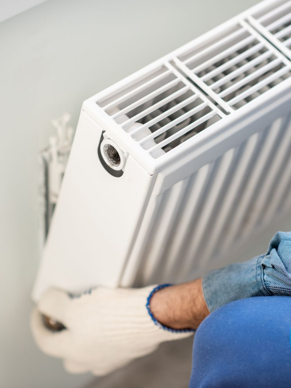Une personne portant des gants installe un radiateur blanc sur un mur.