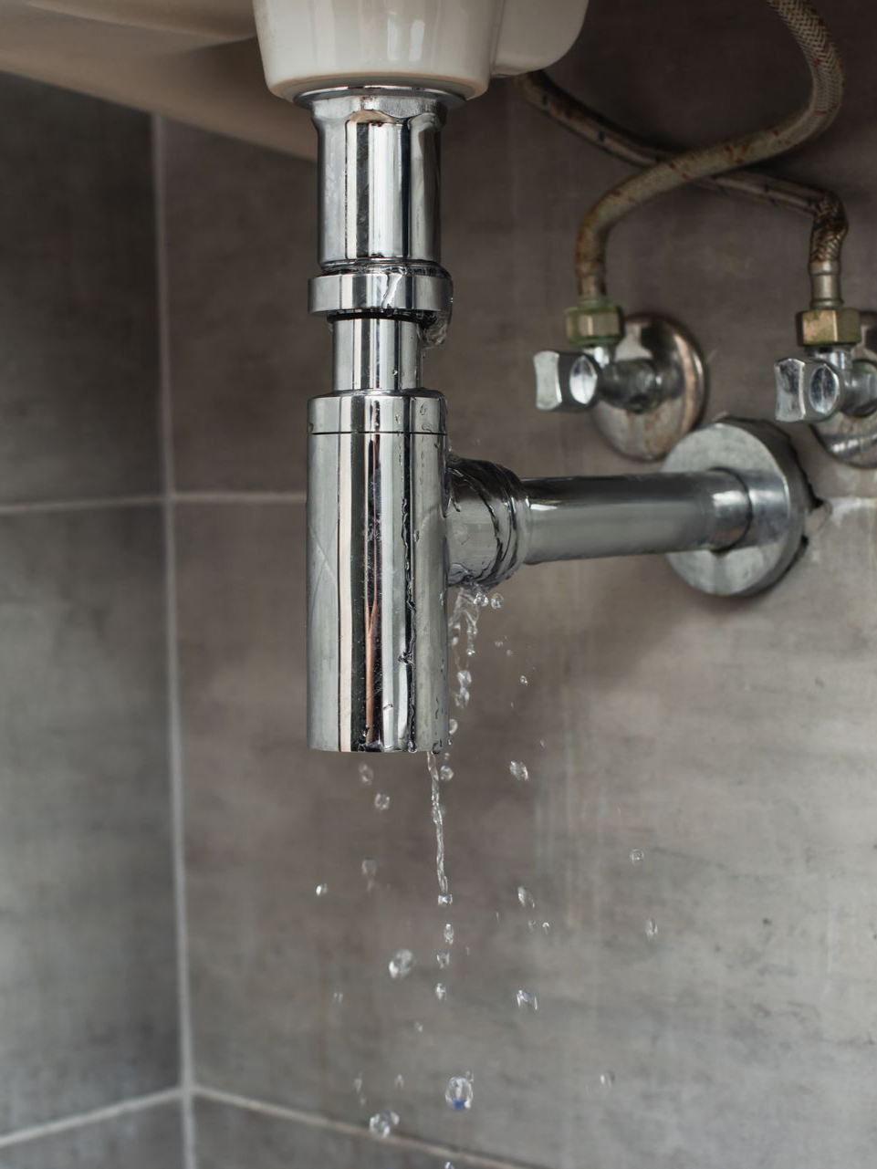 Fuite d'un tuyau d'évier chromé avec des gouttelettes d'eau.