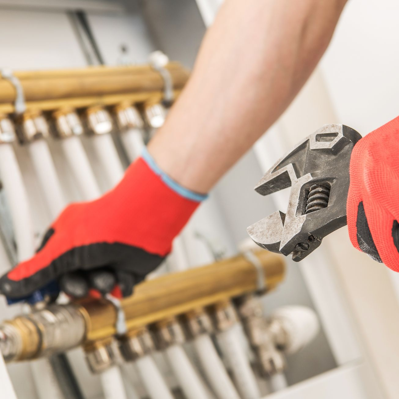 Un plombier portant des gants rouges utilise une clé sur les tuyaux et les vannes.