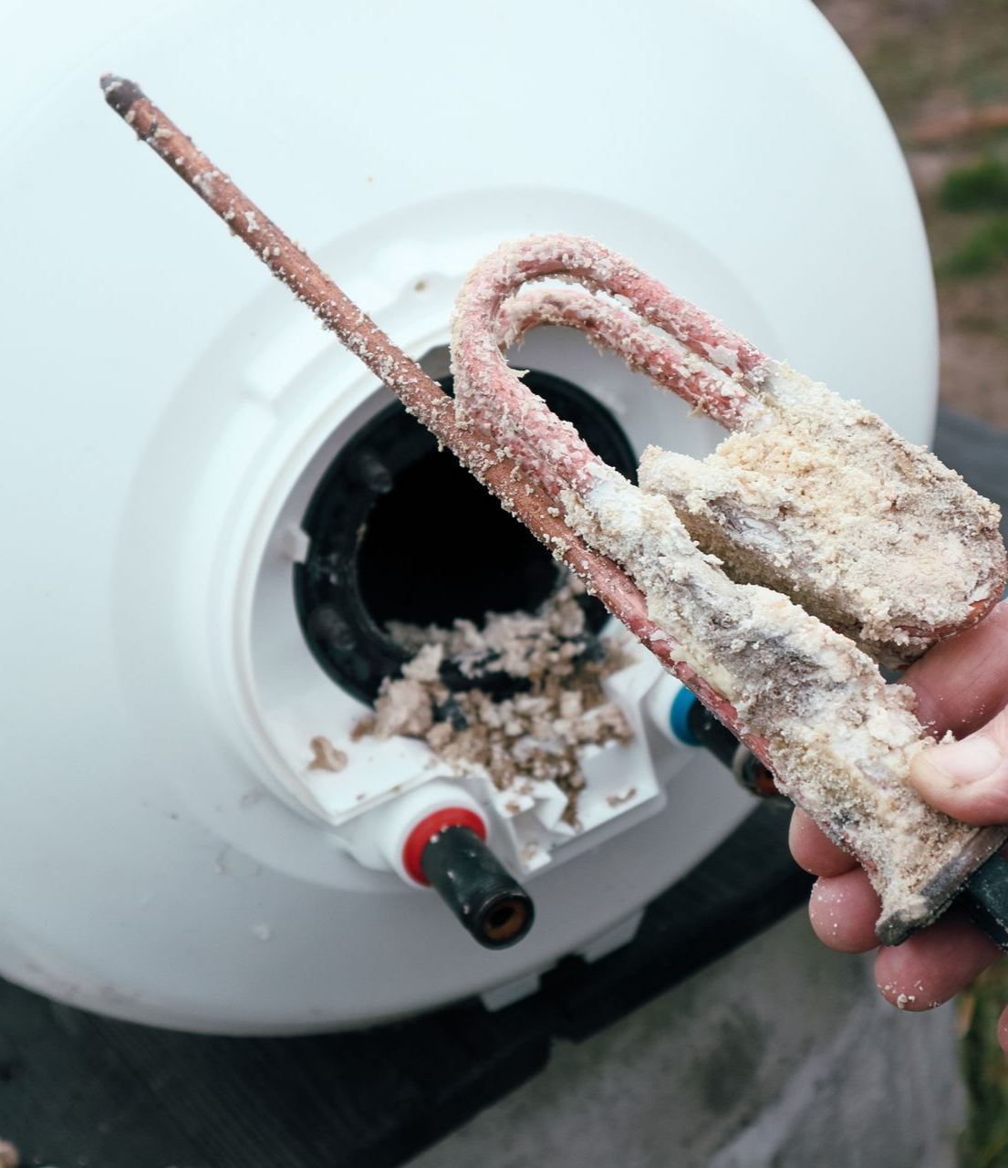 Une personne tient une résistance de chauffe-eau fortement corrodée. Des dépôts blancs recouvrent la résistance.
