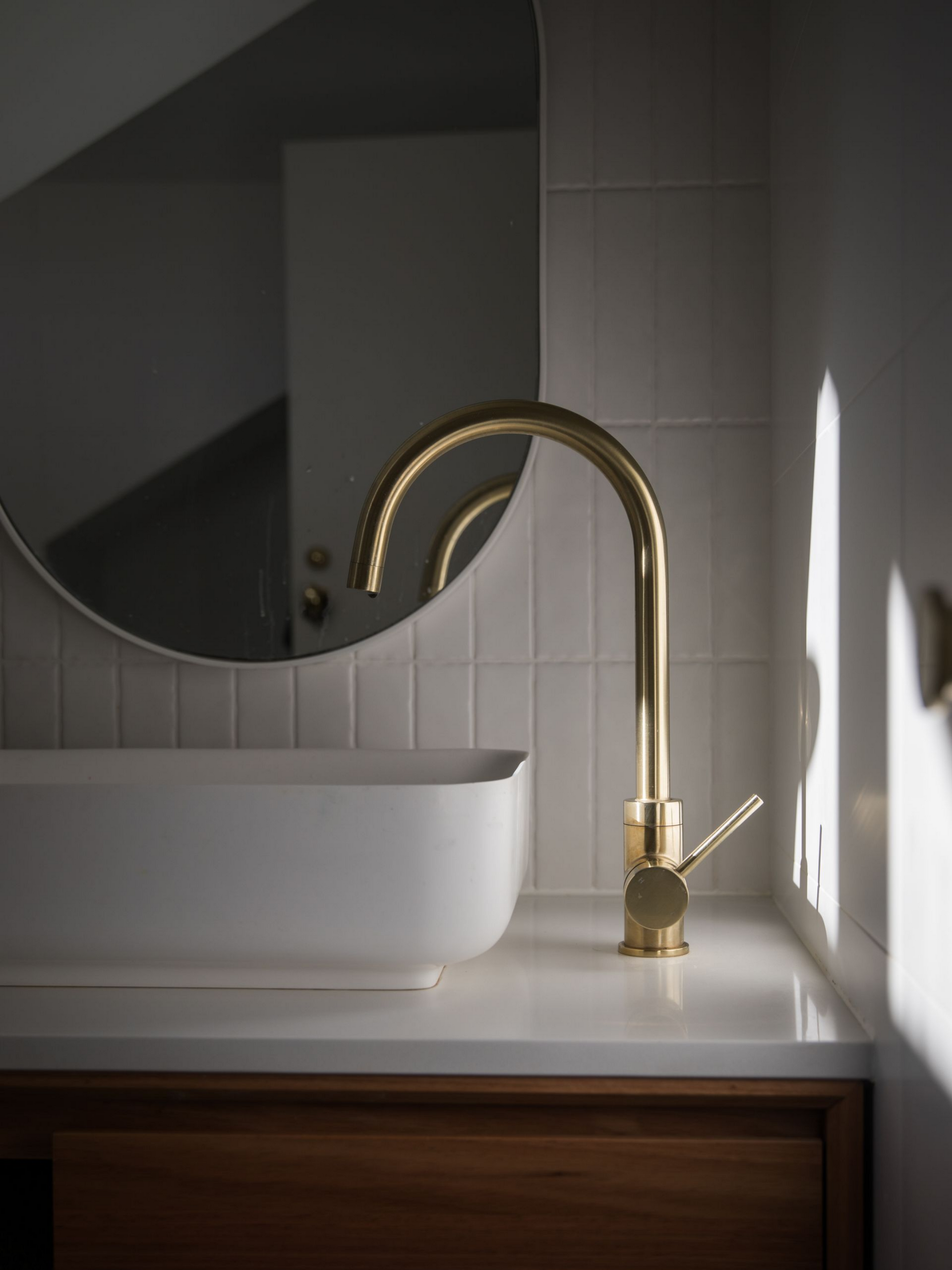 Robinet doré au-dessus d'un lavabo blanc avec miroir rond.