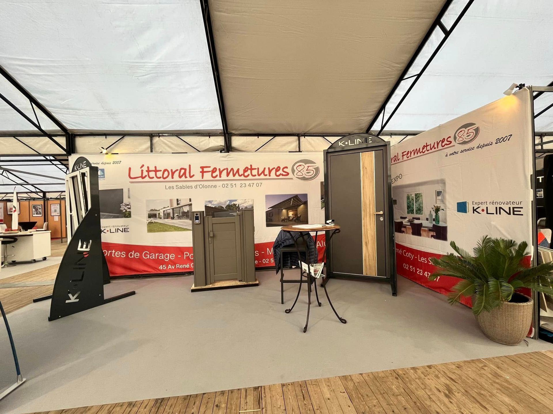 Un stand d'exposition pour Littoral Fermetures, présentant des portes et des cadres de fenêtres sous une grande tente.